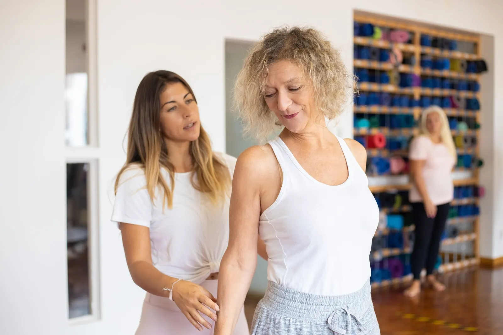 Pilates instructor correcting a client's posture in a bright studio